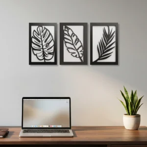 Conjunto de três quadros decorativos em MDF com duas camadas, com desenhos vazados de folhas na cor preto e branco, instalados na parede de um escritório moderno.